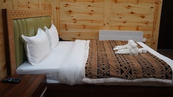 A neatly made bed with white linens and a brown patterned blanket, a wooden headboard, and a small wooden nightstand with a remote control.