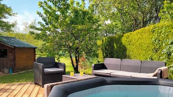 A hot tub with lounge chairs and a table, surrounded by a wooden deck and greenery.
