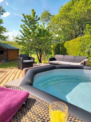 Un bain à remous avec des chaises longues, une terrasse en bois et une zone herbeuse agrémentée d’arbres.