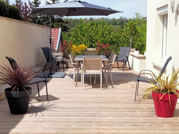 Une terrasse extérieure avec une table et des chaises, entourée de plantes en pot.