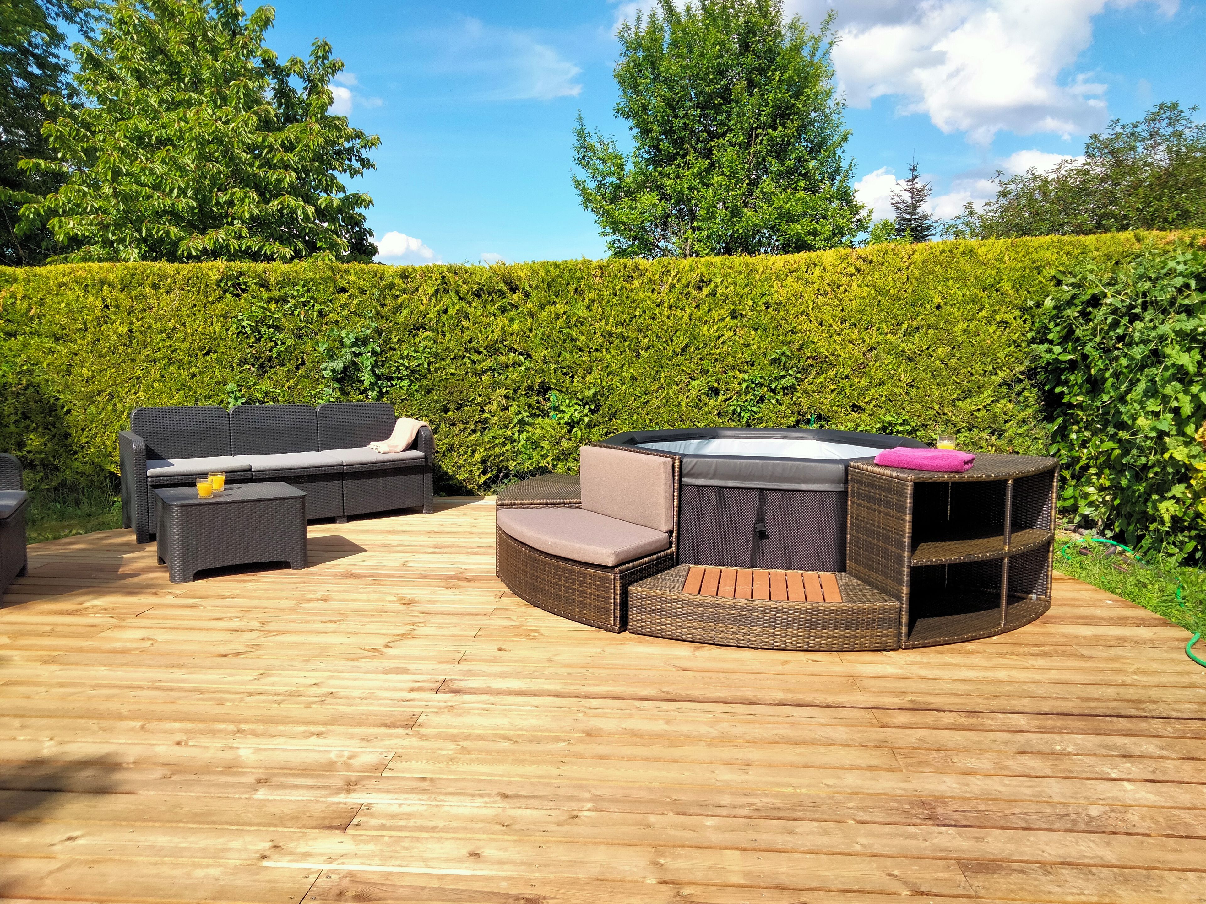 An outdoor patio with wicker furniture, including a sofa and a round table with a hot tub.