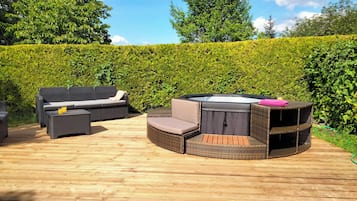 An outdoor patio with wicker furniture, including a sofa and a round table with a hot tub.