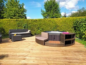 En udendørs terrasse med fletningsmøbler, et spabad og en træterrasse.