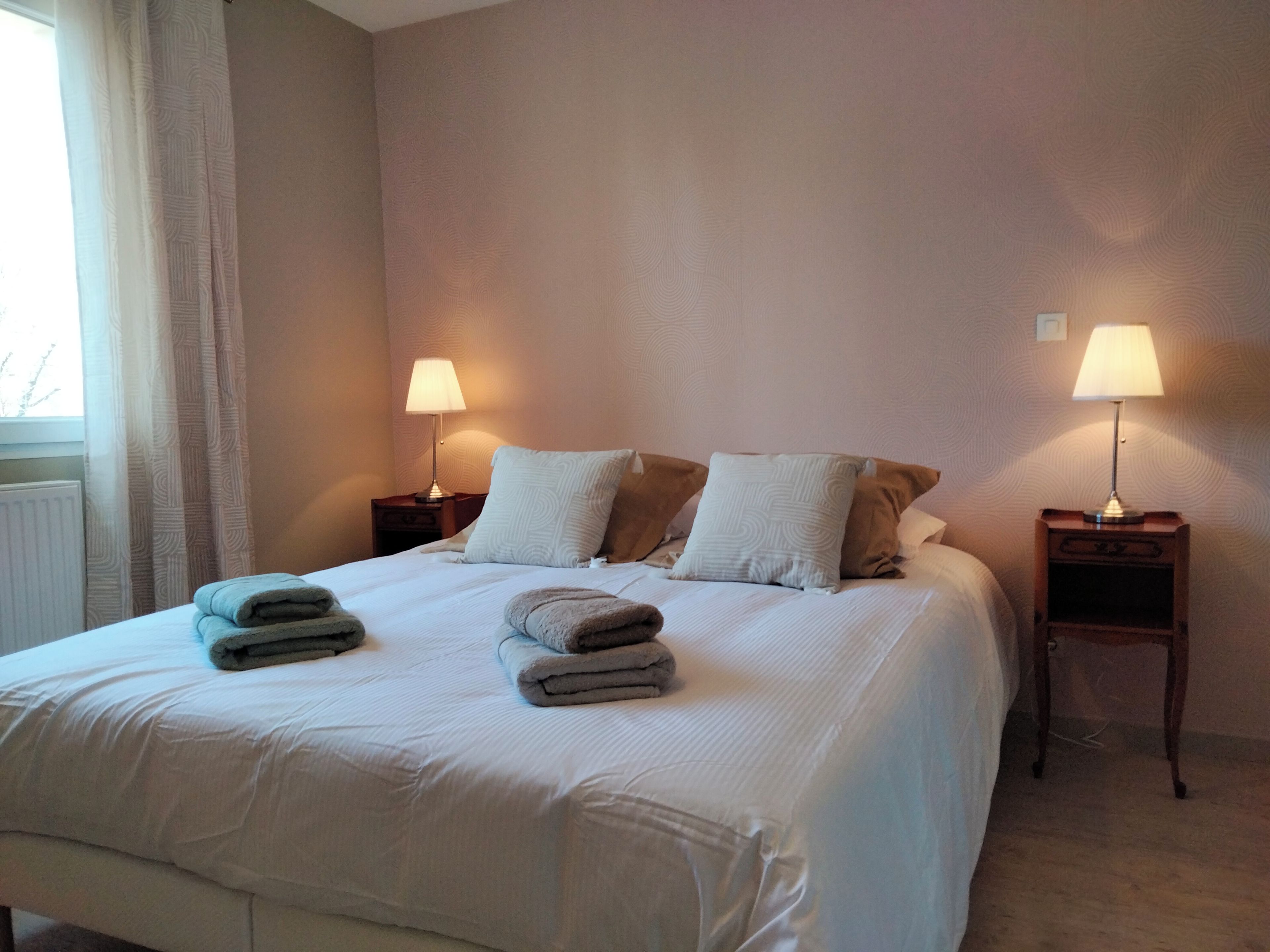 A neatly made bed with two pillows and two folded towels. There are two bedside tables with lamps.