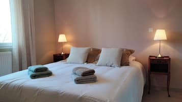 A neatly made bed with two pillows and two folded towels. There are two bedside tables with lamps.
