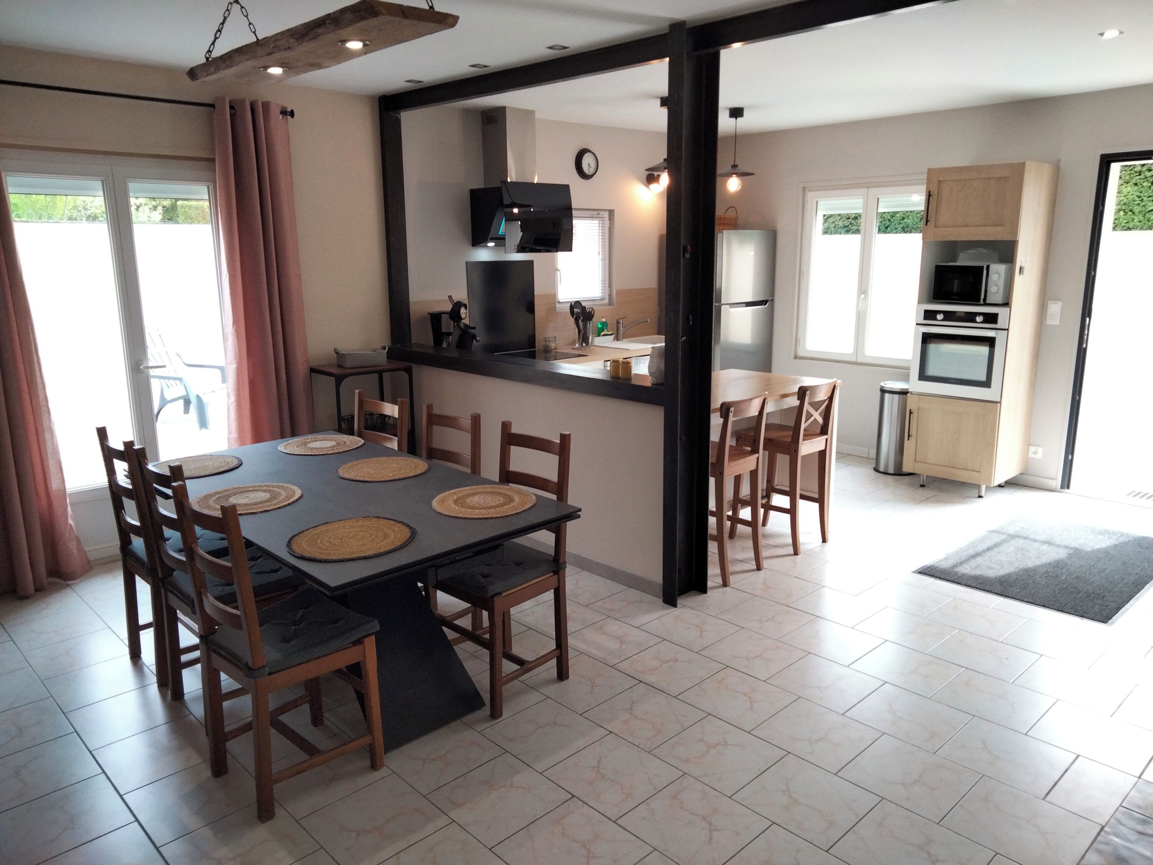 A dining area with a table and chairs, a kitchen with appliances, and a view of the outdoors.