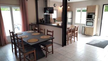 A dining area with a table and chairs, a kitchen with appliances, and a view of the outdoors.
