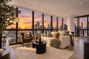 A modern living room with a city skyline view, a sofa, a coffee table, and a potted plant. - Skyline Views | 2 Carpark | Pool, Gym & Spa | Marvel Stadium (Docklands)