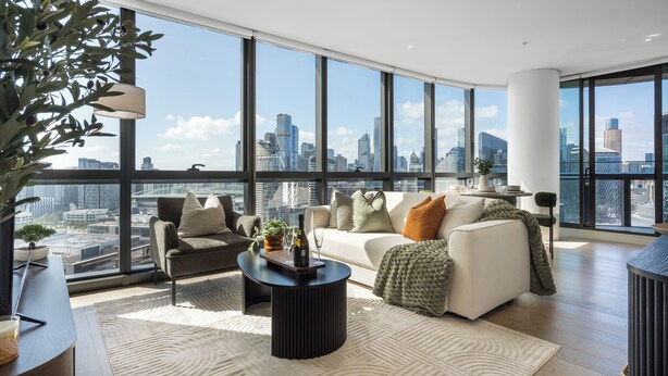 A modern living room with a city view, featuring a sofa, coffee table, and a potted plant. - Designer Apartment | 2 Carpark |Skyline Views | Pool, Gym & Spa | Marvel Stadium (Docklands)