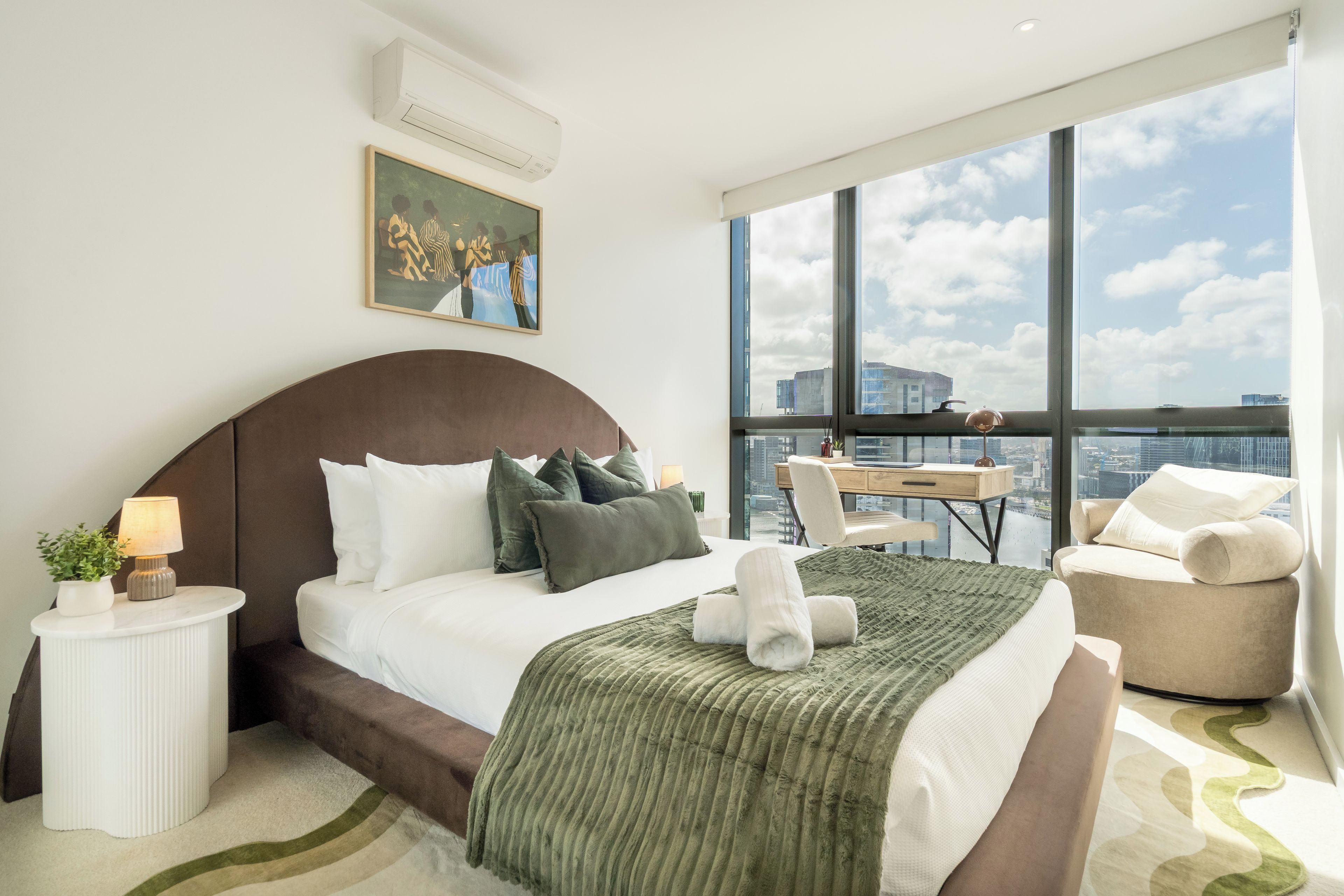 A modern hotel room with a large bed, a desk, and a view of the city.