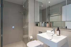 Un bany modern amb dutxa envidriada, un lavabo blanc amb mirall i productes de tocador a la superfície.
