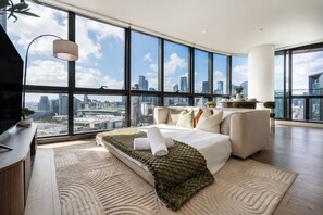 A modern bedroom with a city view, a bed, a desk, and a large window. - Skyline Views | 2 Carpark | Pool, Gym & Spa | Marvel Stadium (Docklands)