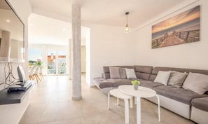 A modern living room with a grey sofa, a small white table, and a painting of a sunset on the wall. - The Shoreline Villa Spacious 4BDR in Caparica (Caparica)