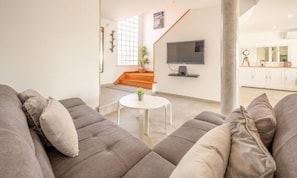A modern living room with a grey sofa, a small white table, and a staircase leading to an upper level. - The Shoreline Villa Spacious 4BDR in Caparica (Caparica)