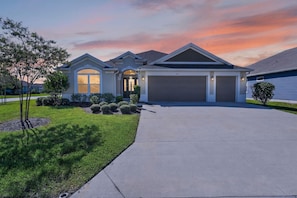 A two-story residential house with a garage, a driveway, and a well-maintained lawn. - Summer Breeze - 3/3 w/ 4-Seat Golf Cart in The Villages - St Catherine (St Catherine, The Villages)