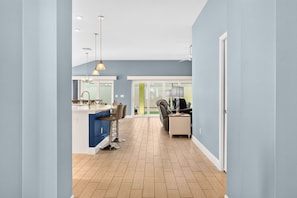 A modern kitchen with a blue countertop, a dining area with chairs, and a view to the outside. - Summer Breeze - 3/3 w/ 4-Seat Golf Cart in The Villages - St Catherine (St Catherine, The Villages)