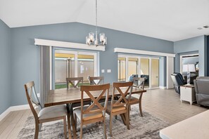 A dining area with a wooden table and chairs, a chandelier, and large windows with curtains. - Summer Breeze - 3/3 w/ 4-Seat Golf Cart in The Villages - St Catherine (St Catherine, The Villages)