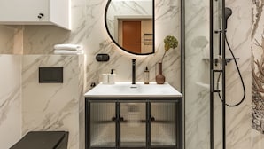 Un baño moderno con pared de mármol, un espejo redondo, cabina de ducha y un armario con marco negro.