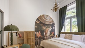 Un dormitorio con cama, escritorio con lámpara, silla, estantería y un mural grande en la pared.