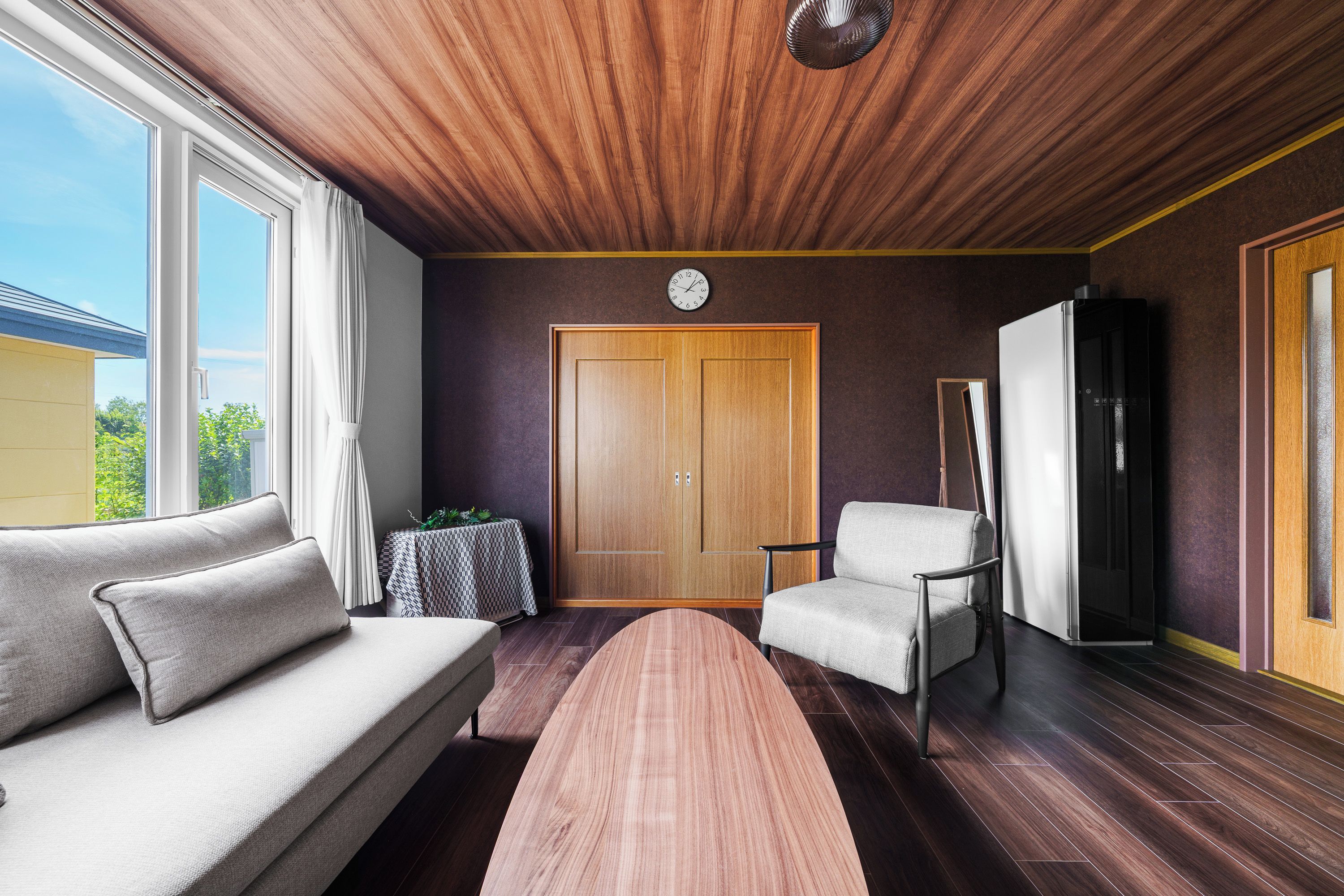 Un interior moderno con techo de madera, un sofá, una silla, una mesa y un refrigerador.