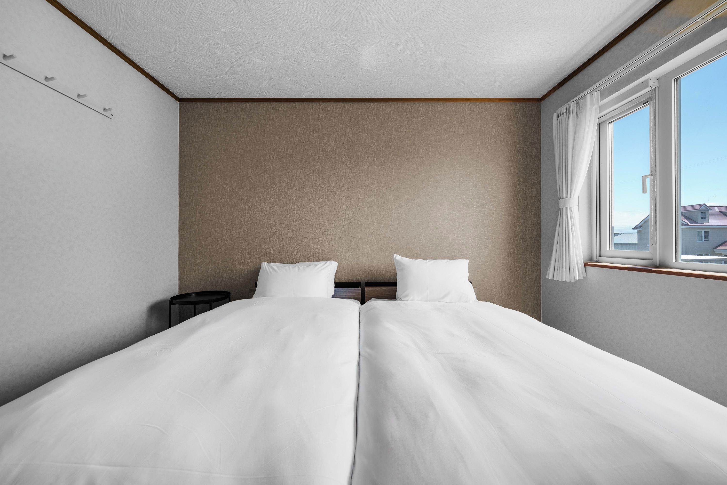 A twin bed with white bedding in a room with a window, a small table, and a patterned wall.
