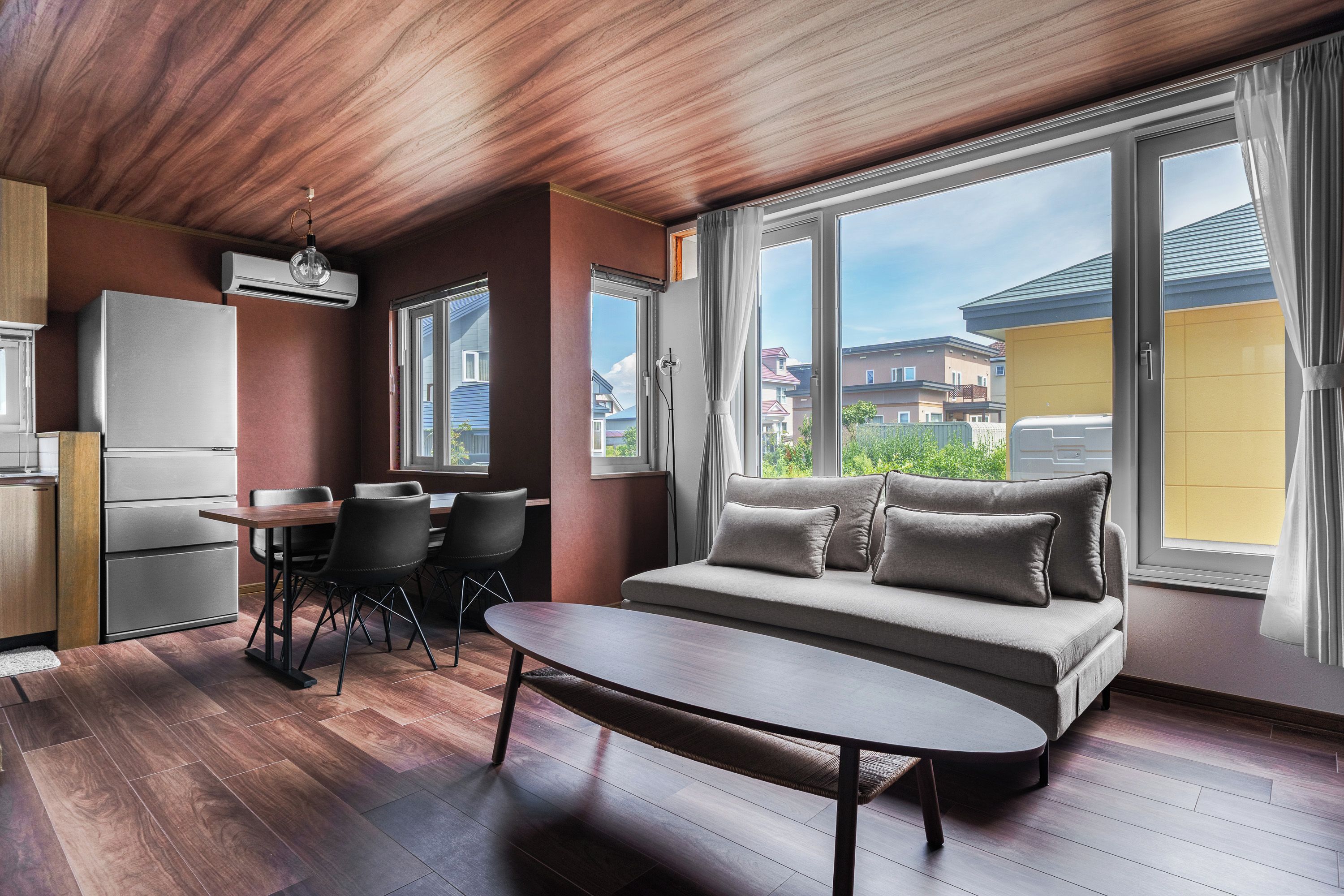 Una sala de estar moderna con sofá, mesa de comedor, sillas y una zona de cocina con refrigerador.