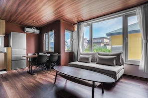 A modern living room with a sofa, dining table, chairs, and a kitchen area with a refrigerator. - PRIVATE VILLA BIEI (Biei)
