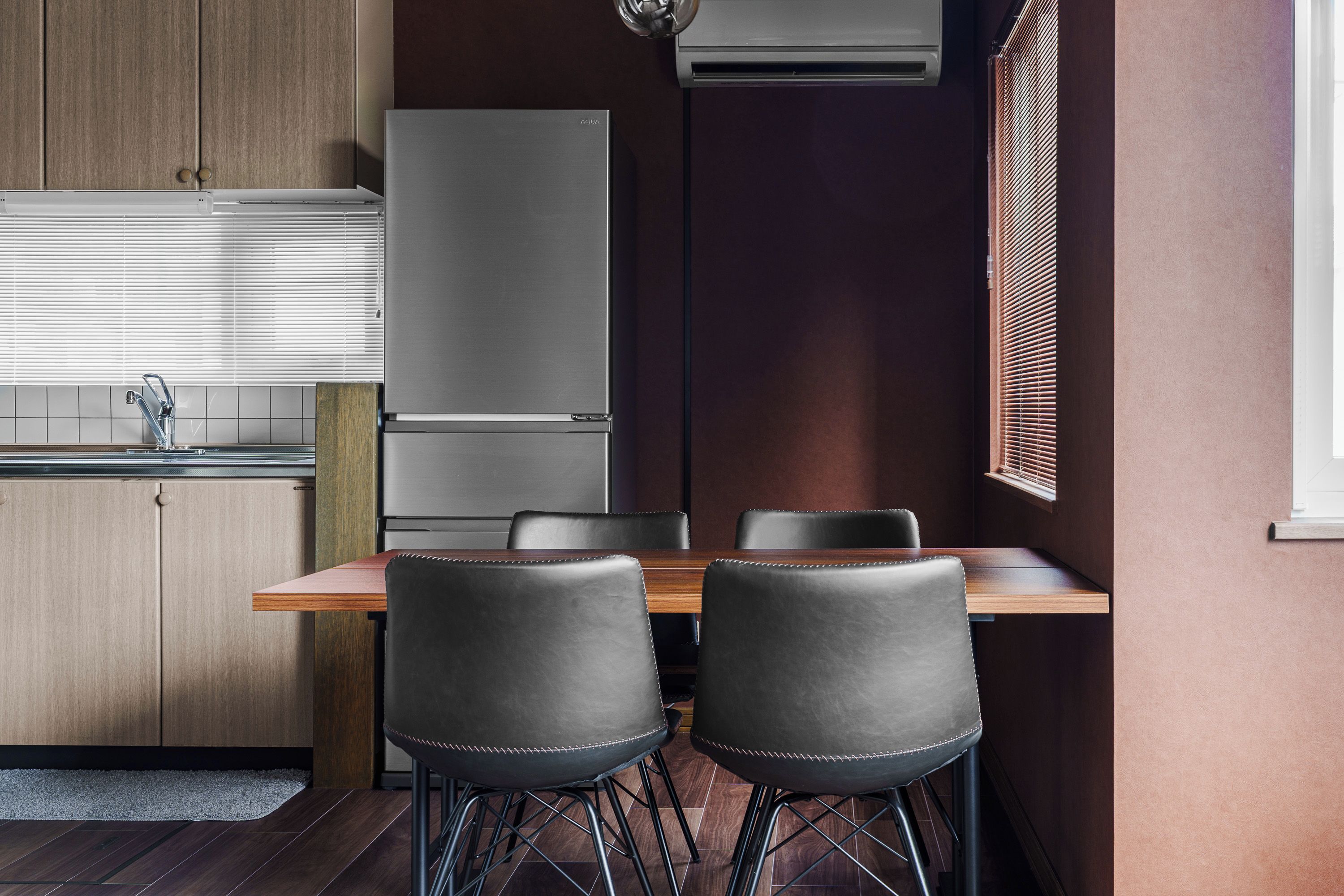 Una cocina moderna con refrigerador empotrado, una mesa de comedor con sillas y un ventanal con persianas.