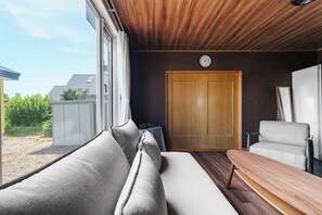 Una habitación con techo de madera, un ventanal grande, una puerta y una zona de estar con un banco y un sofá.