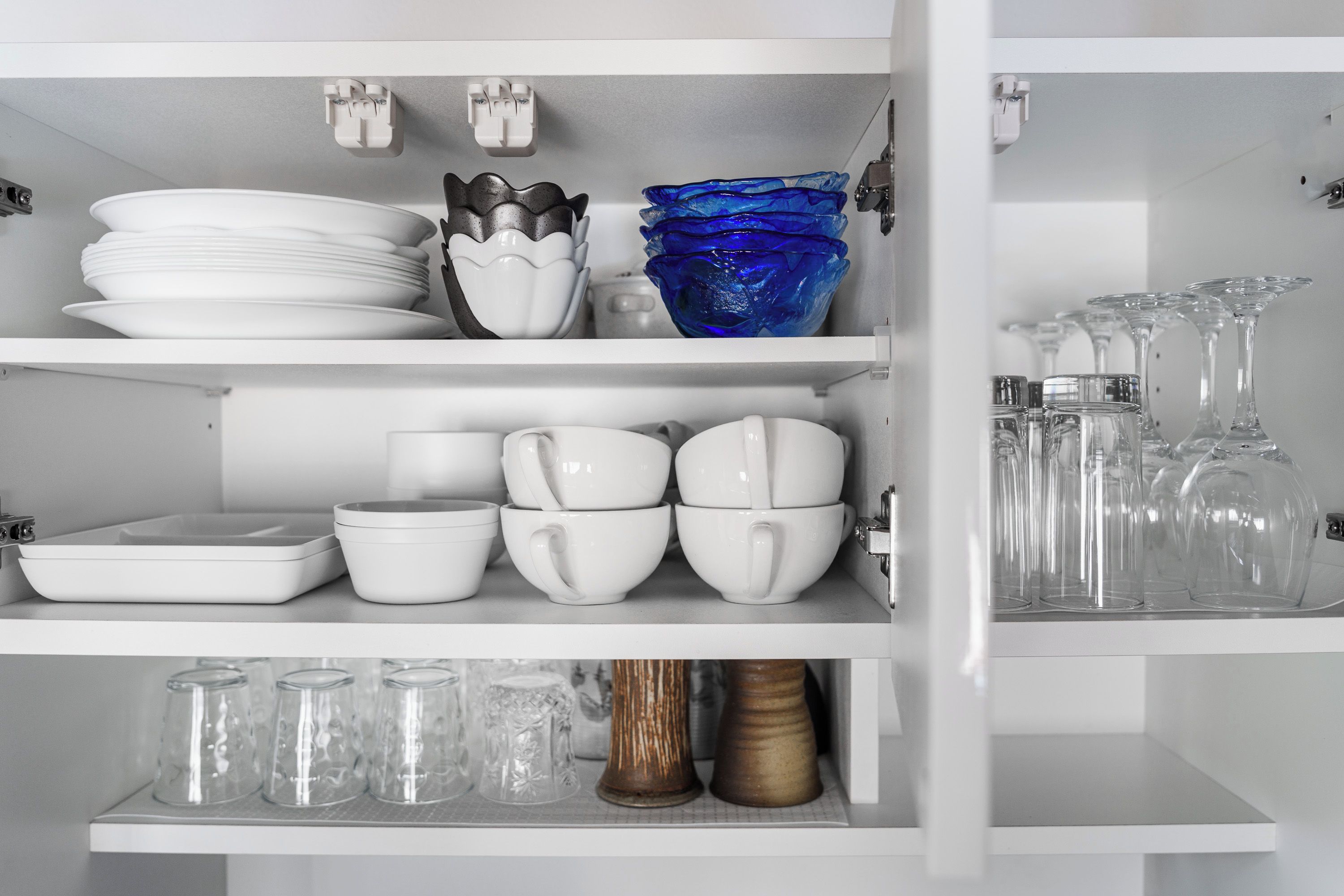 Un armario de cocina con platos, tazones, vasos y copas blancos.