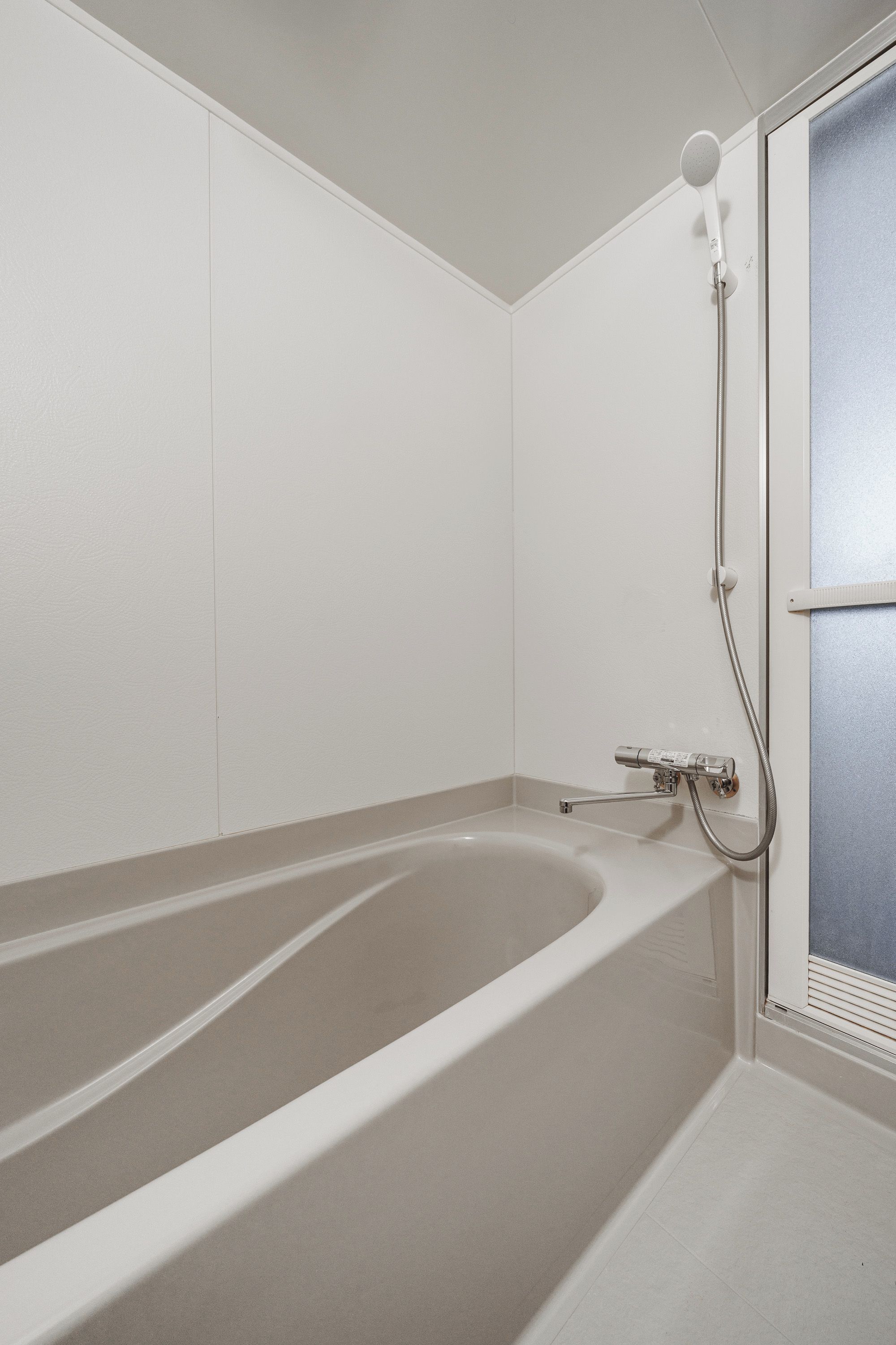 A bathroom with a freestanding bathtub, a showerhead, and a window with blinds.