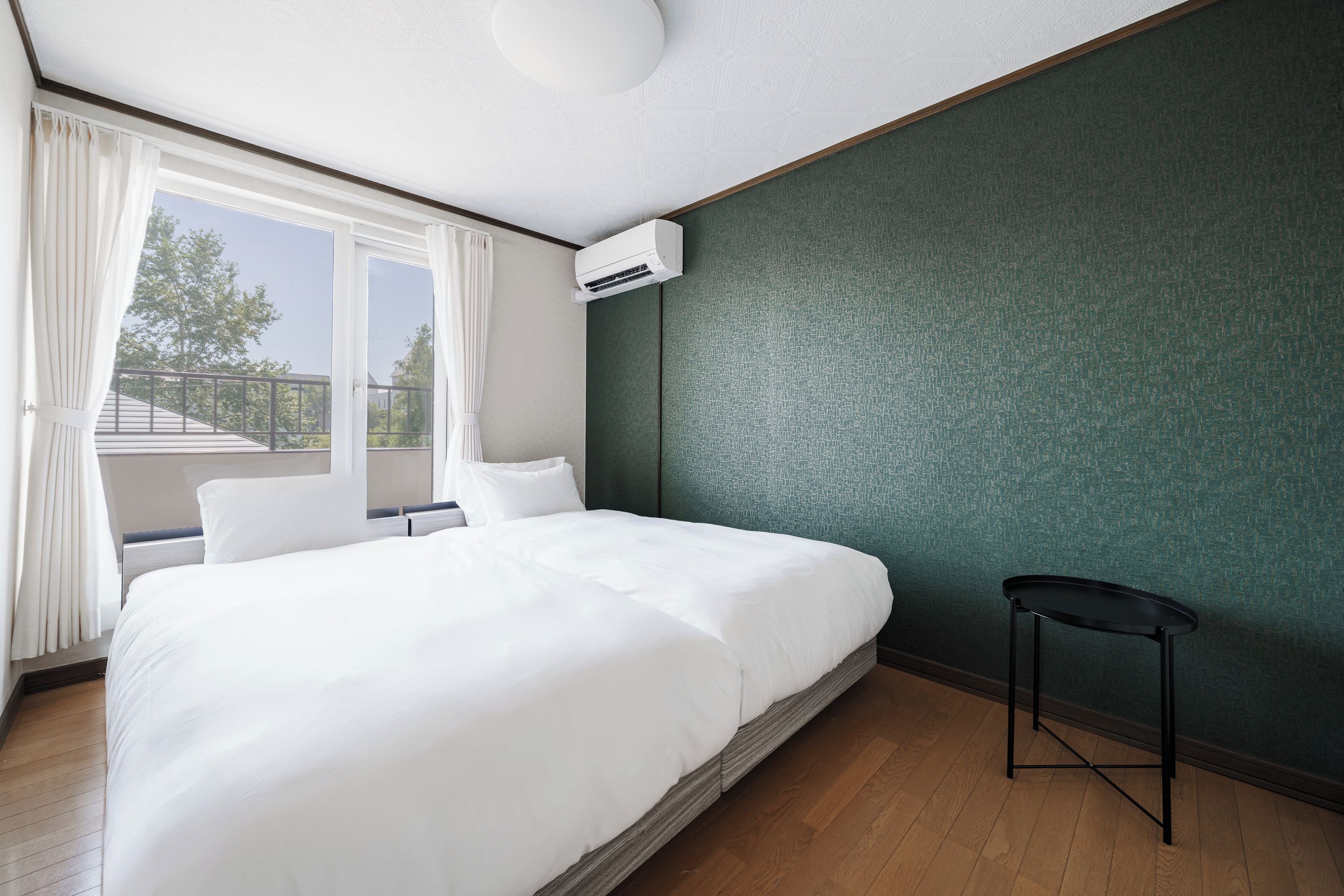 Quarto de hotel com uma cama grande, uma mesinha de cabeceira pequena, uma janela com cortinas e um ar condicionado.