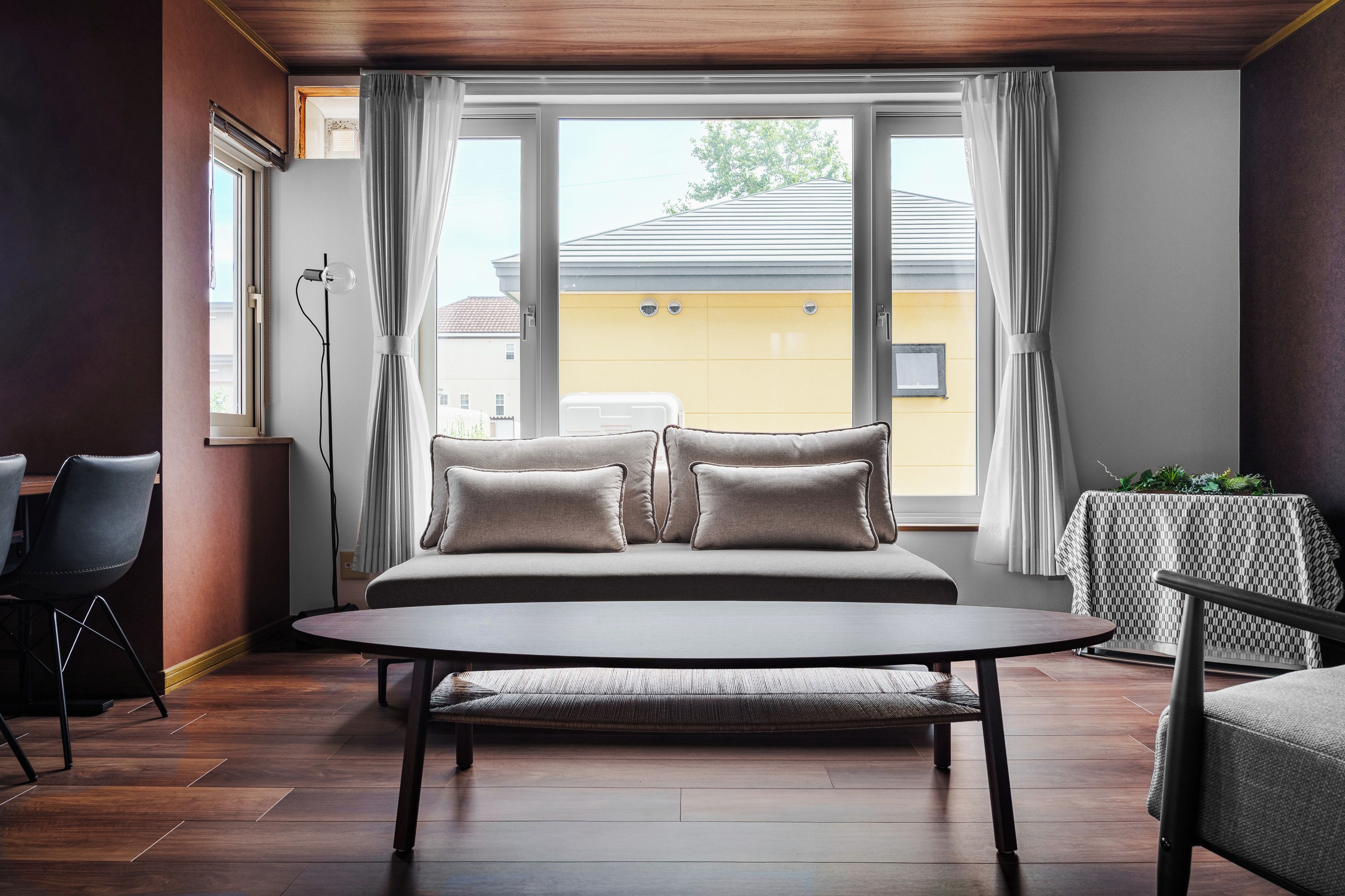 A modern bedroom with a large bed, a bedside table, a chair, and a view of a yellow building through the window.