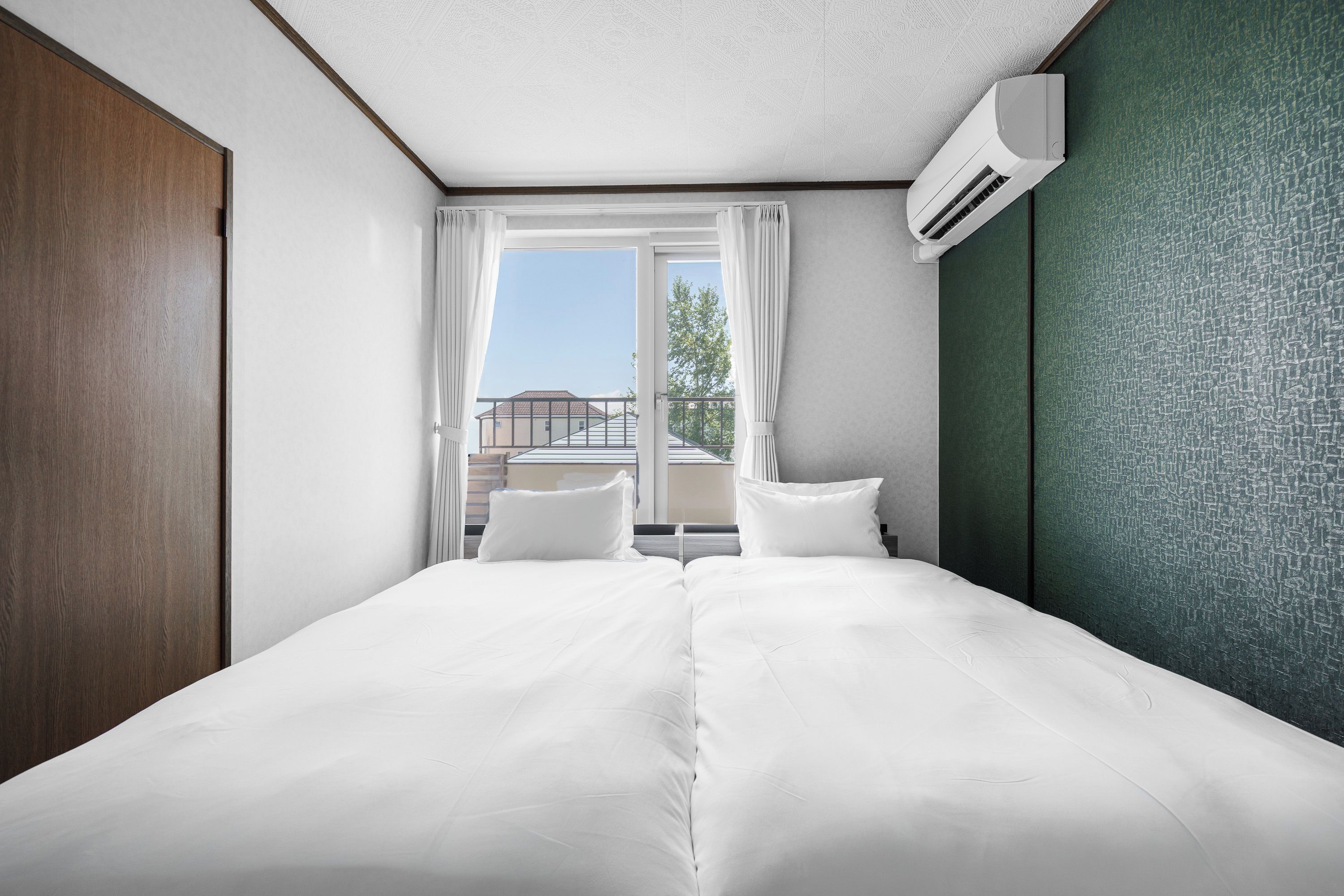 A hotel room with a bed, two pillows, a window with curtains, and an air conditioning unit.