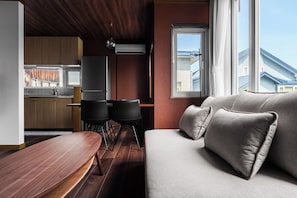 Un interior moderno con una mesa de comedor de madera, un sofá con cojines y una cocina con armarios y ventana.