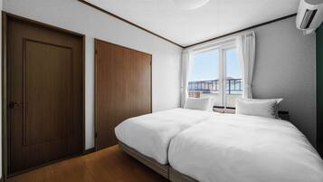 A hotel room with a large bed, a wardrobe, a window with curtains, and an air conditioning unit.