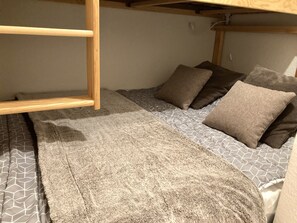 Een stapelbed met een houten ladder, een grijs beddegoed met patroon en meerdere kussens.