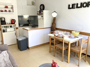 Eine kompakte Küche mit Essbereich, einer Kaffeemaschine, einem Wasserkocher und einer kleinen Mülltonne.