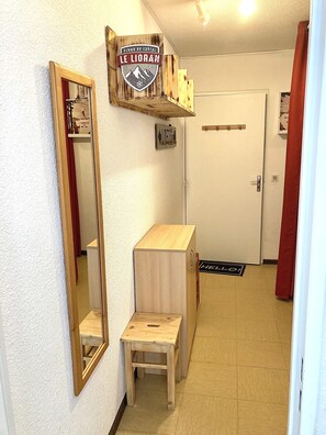 Ein Flur mit einem Holzkasten, einem Spiegel und einer Tür mit einer Fußmatte, auf der 'HELLO!' steht.