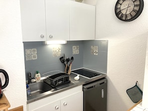 Een kleine keuken met witte kastjes, een zwarte kookplaat en een spoelbak.