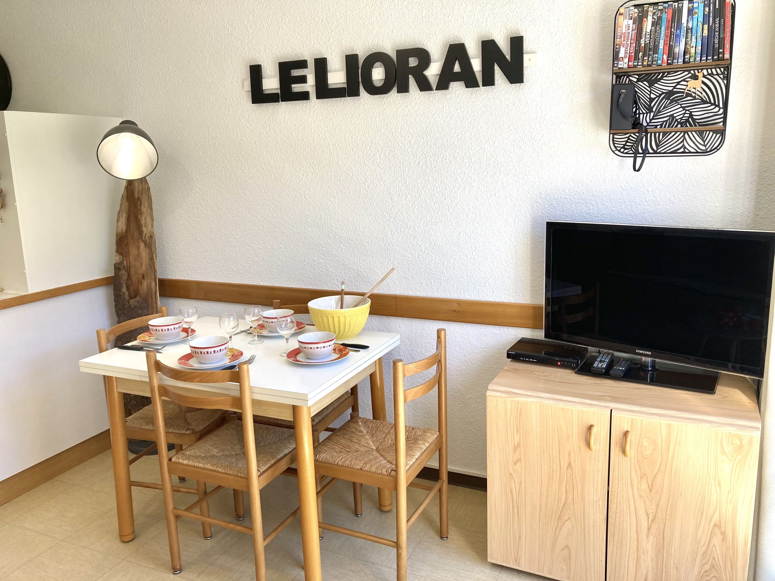 Zona pranzo con tavolo apparecchiato per due, televisione e libreria piena di libri.