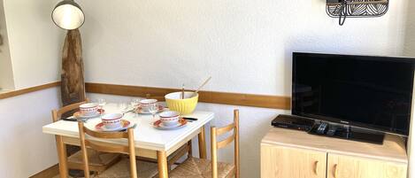 Zona pranzo con tavolo apparecchiato per due, televisione e libreria piena di libri.