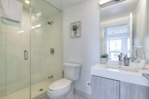 Une salle de bain moderne avec une douche en verre, des toilettes blanches, un lavabo avec un miroir et une petite plante en pot.