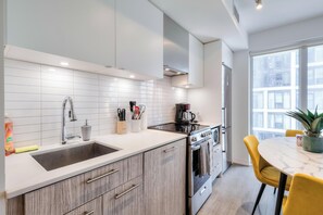 Une cuisine moderne avec un évier en acier inoxydable, des armoires en bois et un coin repas comprenant une table ronde et des chaises jaunes.