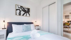 Habitació d'hotel amb un llit, taules de nit, una obra d'art abstracta penjada a la paret i vista a la zona de dinar adjacenta.