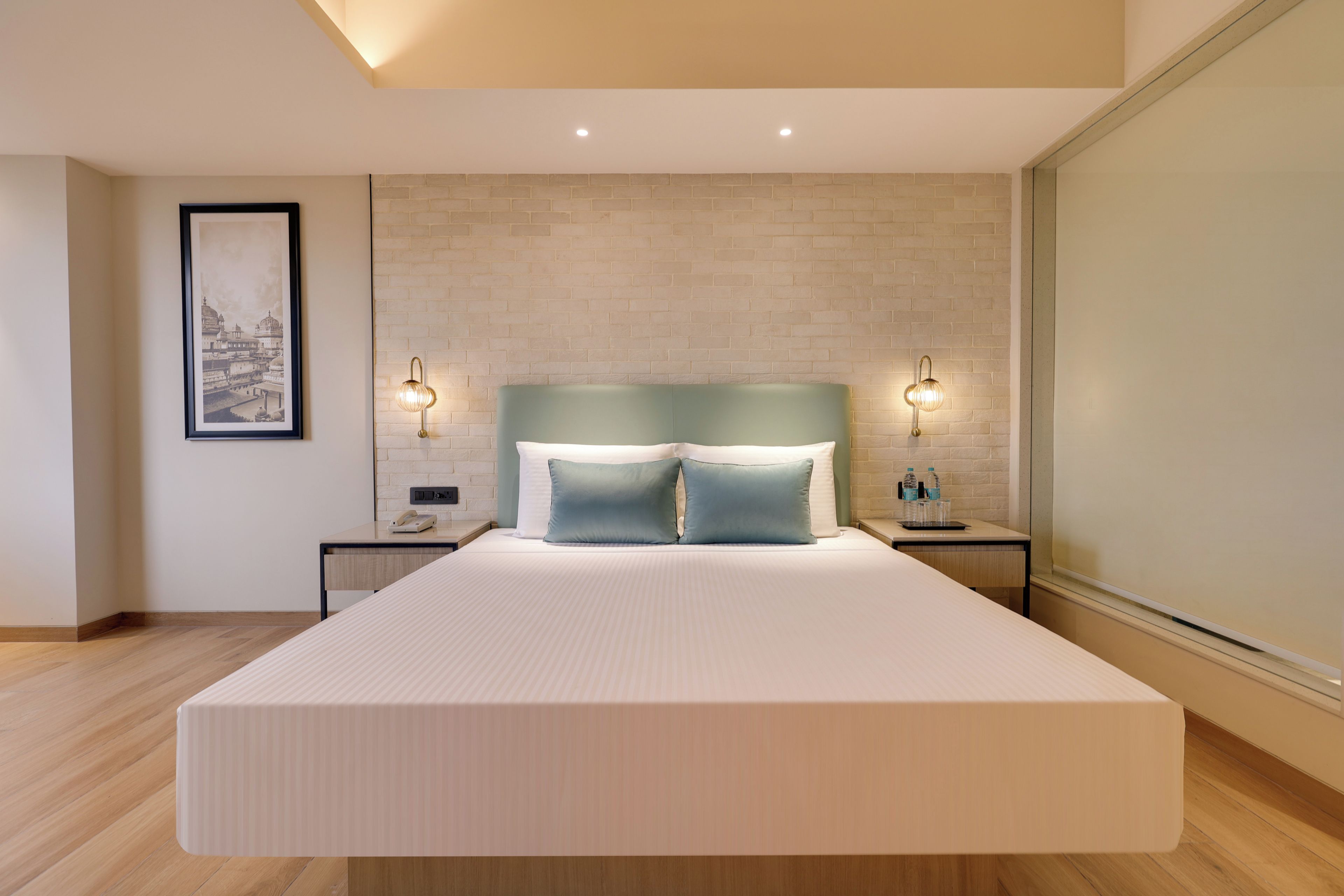 A modern bedroom with a large bed, two bedside tables, a nightstand, a framed picture on the wall, and a brick-patterned wall.