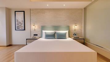 A modern bedroom with a large bed, two bedside tables, a nightstand, a framed picture on the wall, and a brick-patterned wall.