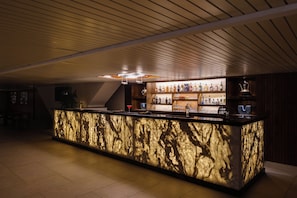 Un área de bar con mostrador de mármol, estantes con botellas y techo de madera.
