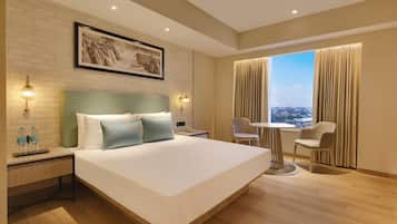 A hotel room with a large bed, a desk, a chair, a view of the city, and a brick wall.