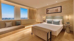 A modern hotel room with a large bed, a sofa, a view of the city, and a brick wall. - Lemon Tree Premier, Jabalpur (Jabalpur)